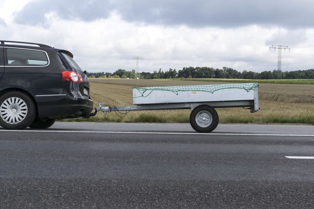 Black Car Towing a Small White Trailer on a Road — Hinterland Towbar & Steel Fabrication In Yandina, QLD