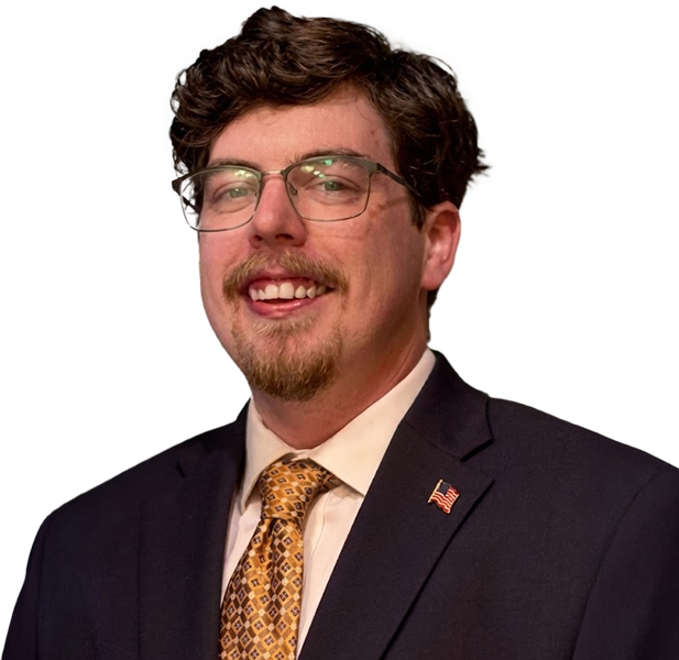 Man in suit and glasses smiling at the camera; gold patterned tie; American flag pin.
