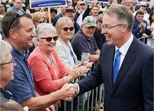 Man in a blue suit speaks at a press conference outdoors, with microphones in front of him.