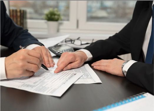 Two people in suits reviewing documents at a desk, one pointing with a finger and the other holding a pen.
