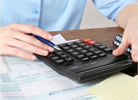 Person using a calculator, likely doing taxes. Paperwork and sticky notes are present.