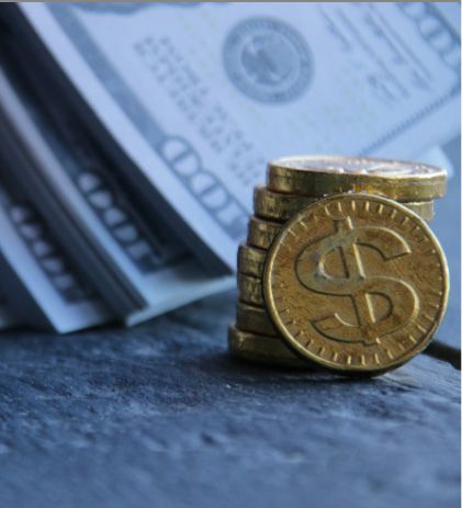Stack of gold coins with dollar symbol next to a stack of hundred-dollar bills.