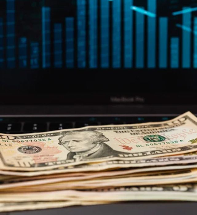 Stack of US ten-dollar bills on a laptop keyboard; stock market graph displayed on the screen.