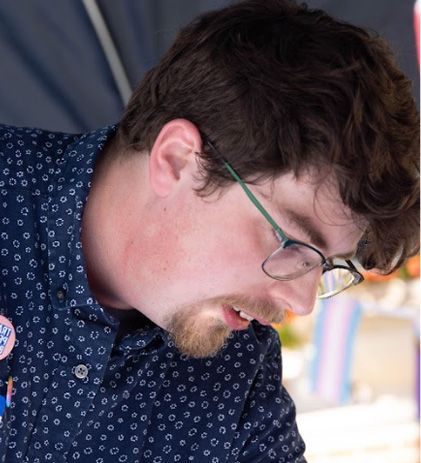 Man with glasses looking down, wearing blue patterned shirt.