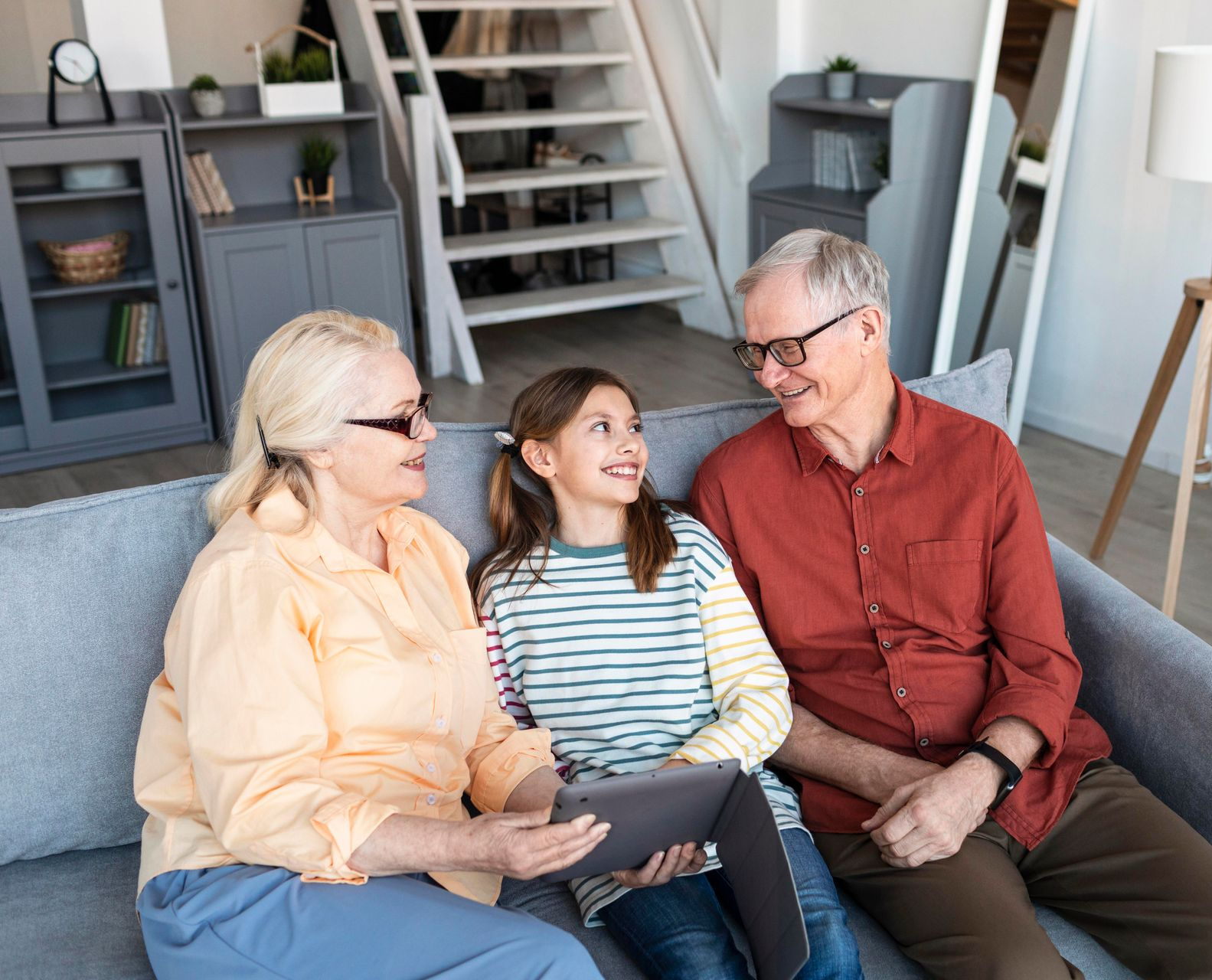 Woman in white shirt sits on a sofa, hands clasped. Reflection visible on a table.