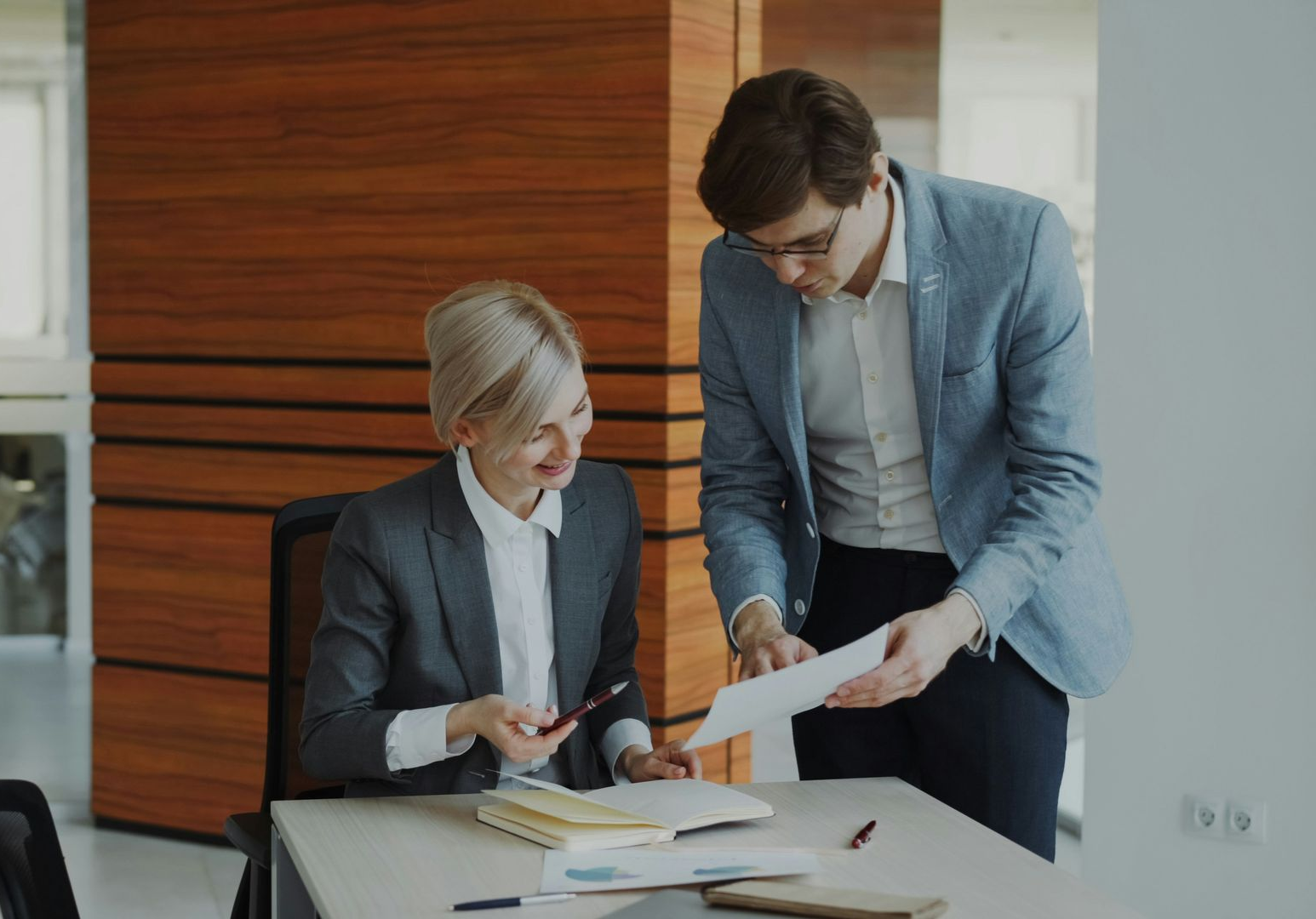 Woman in white shirt sits on a sofa, hands clasped. Reflection visible on a table.