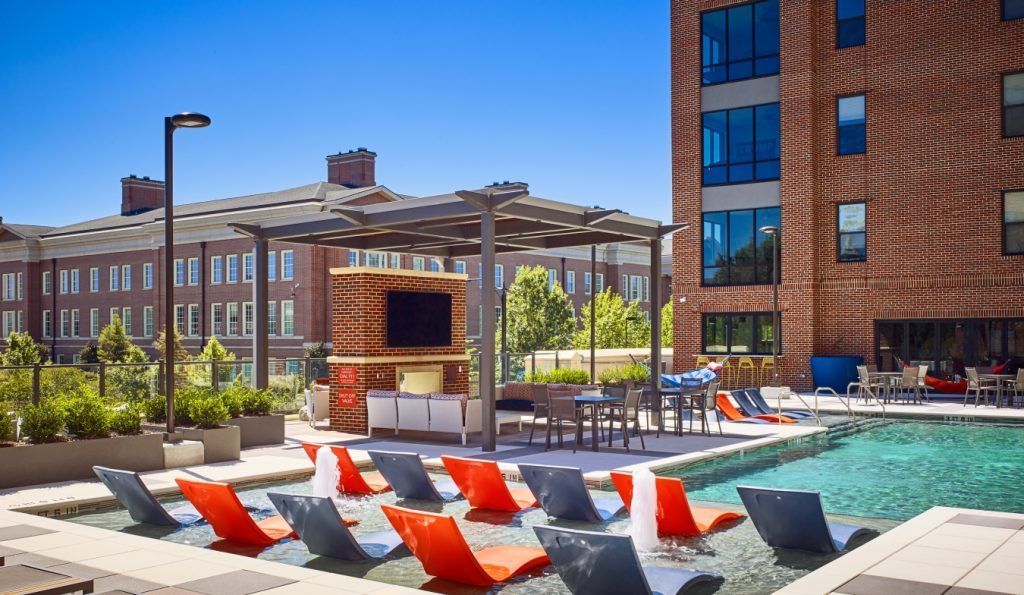 A large swimming pool surrounded by chairs and tables in front of a brick building.