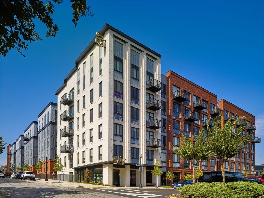 A large building with a lot of windows is surrounded by other buildings on a sunny day.