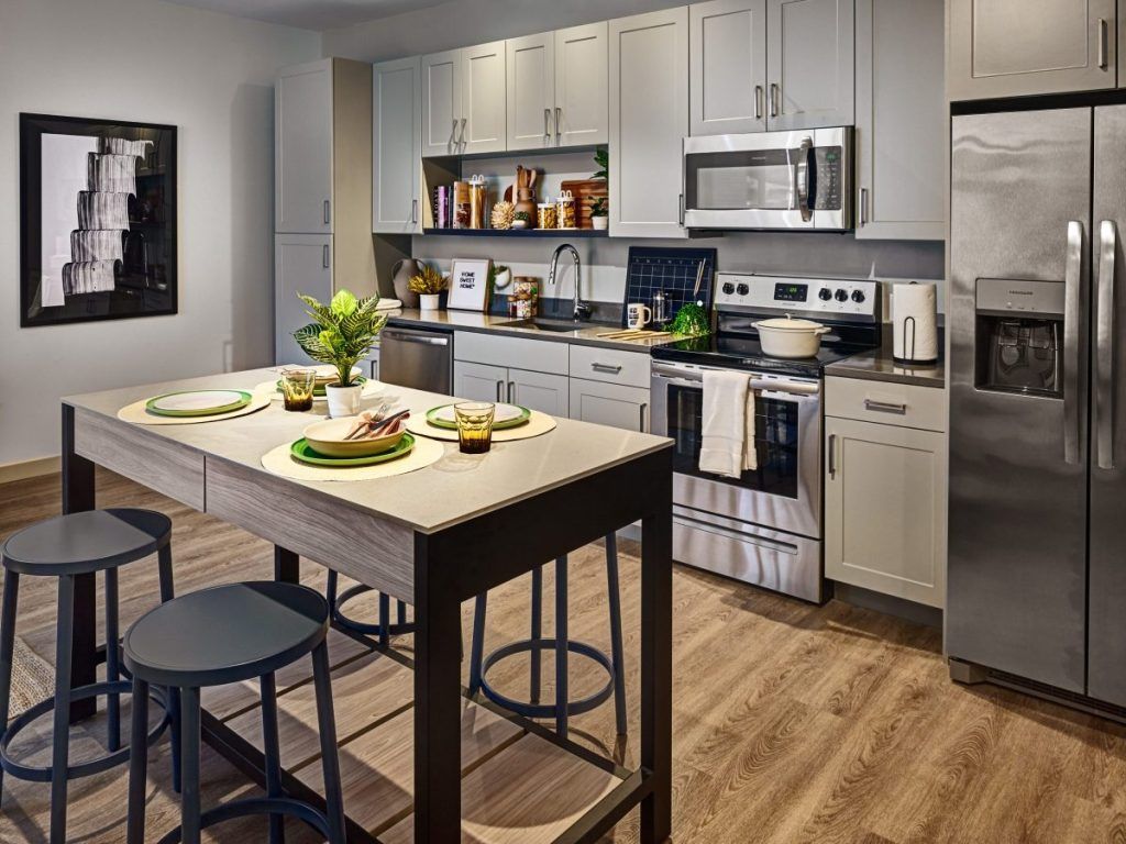 A kitchen with stainless steel appliances , white cabinets , a table and stools.
