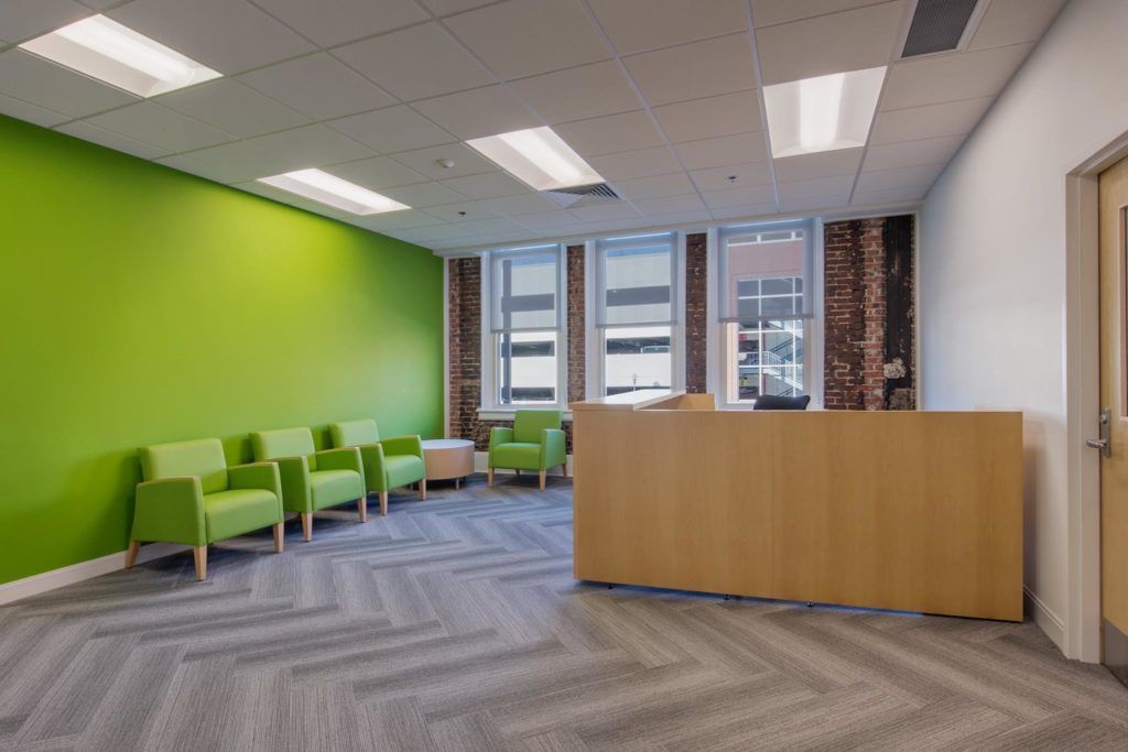 A waiting room with green chairs and a wooden counter.