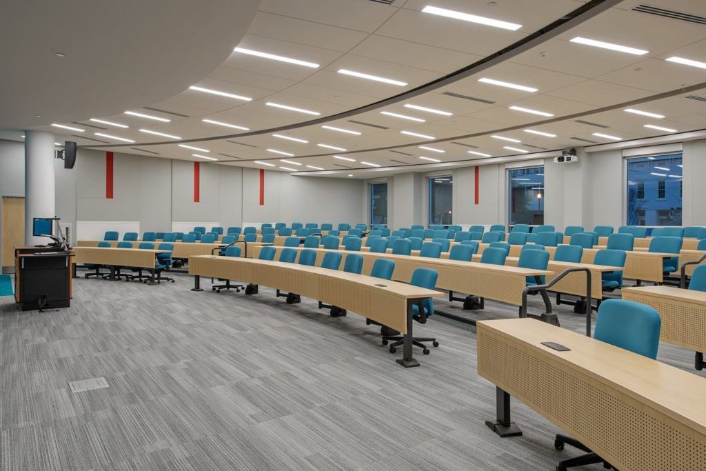 A large lecture hall with tables and chairs in it.