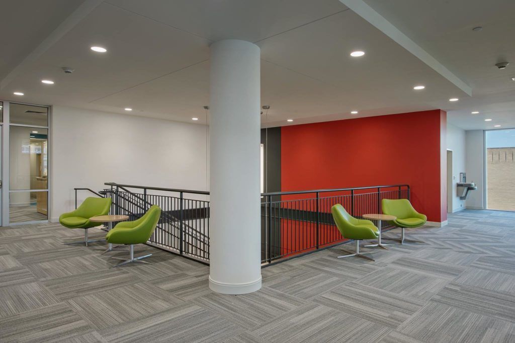 A hallway with green chairs and tables and a red wall.