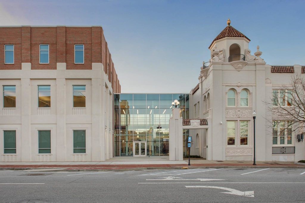 A large building with a lot of windows is next to a smaller building.