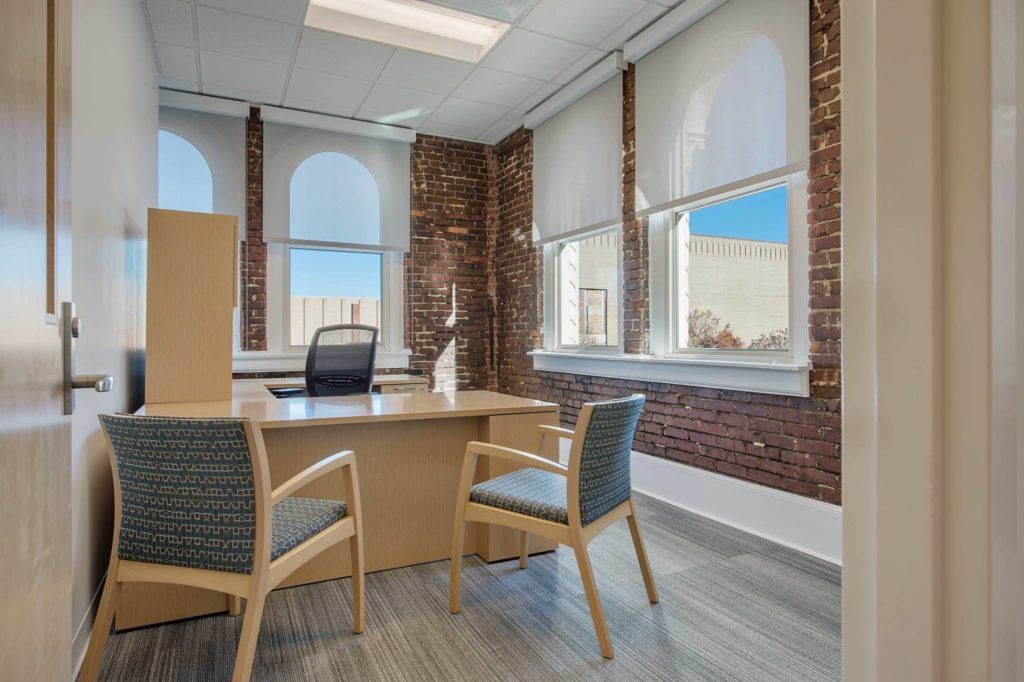 A small office with a desk , chairs , and windows.