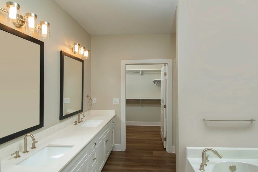 A bathroom with two sinks , two mirrors and a walk in closet.