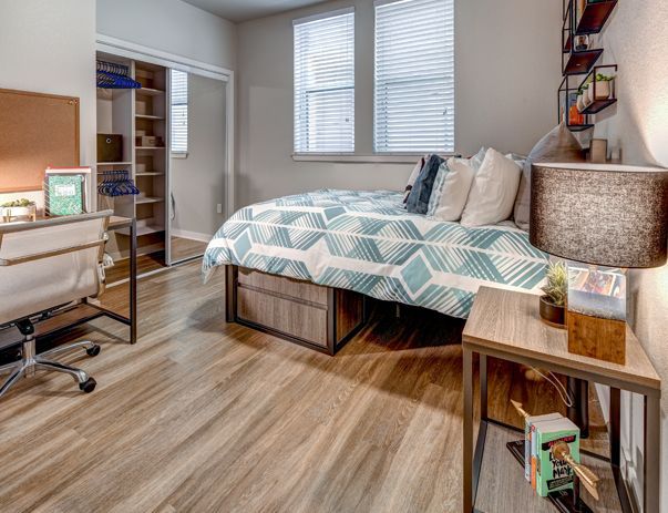 A bedroom with a bed , desk , nightstand and lamp.