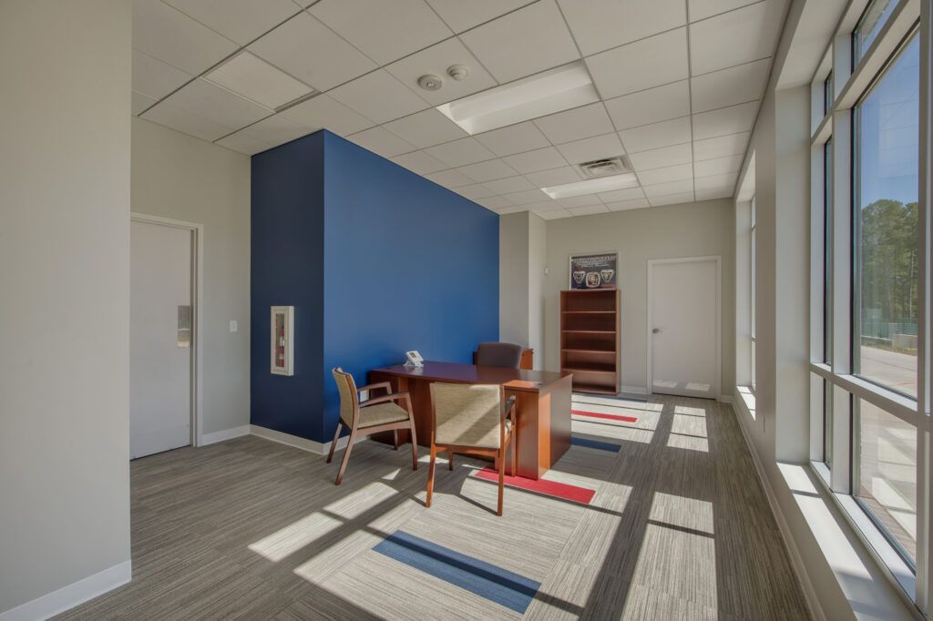 A room with a desk and chairs in it and a blue wall.