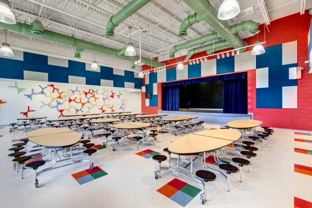 A school cafeteria with tables and chairs and a stage.