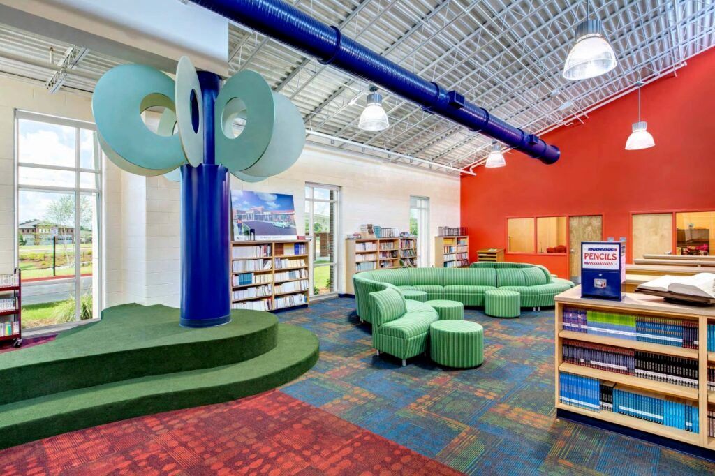 A library with a green couch , ottomans , shelves and a blue pillar.
