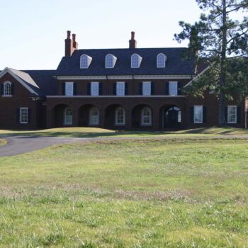 A large brick building with arched windows sits in the middle of a grassy field