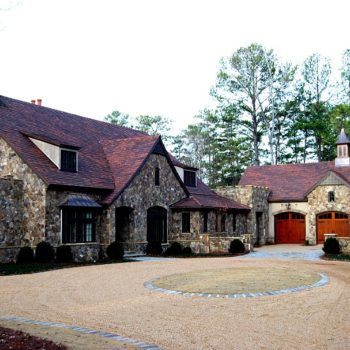 A large stone house with a red roof and two garages