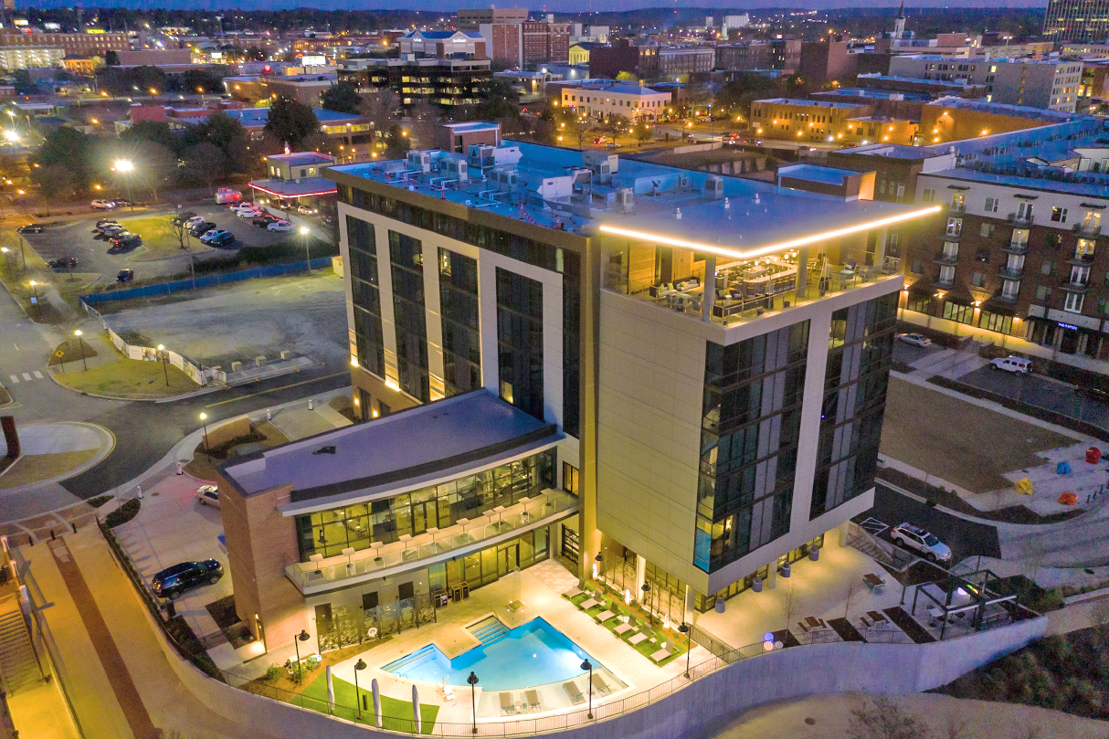 An aerial view of a hotel with a pool in the middle of a city at night.