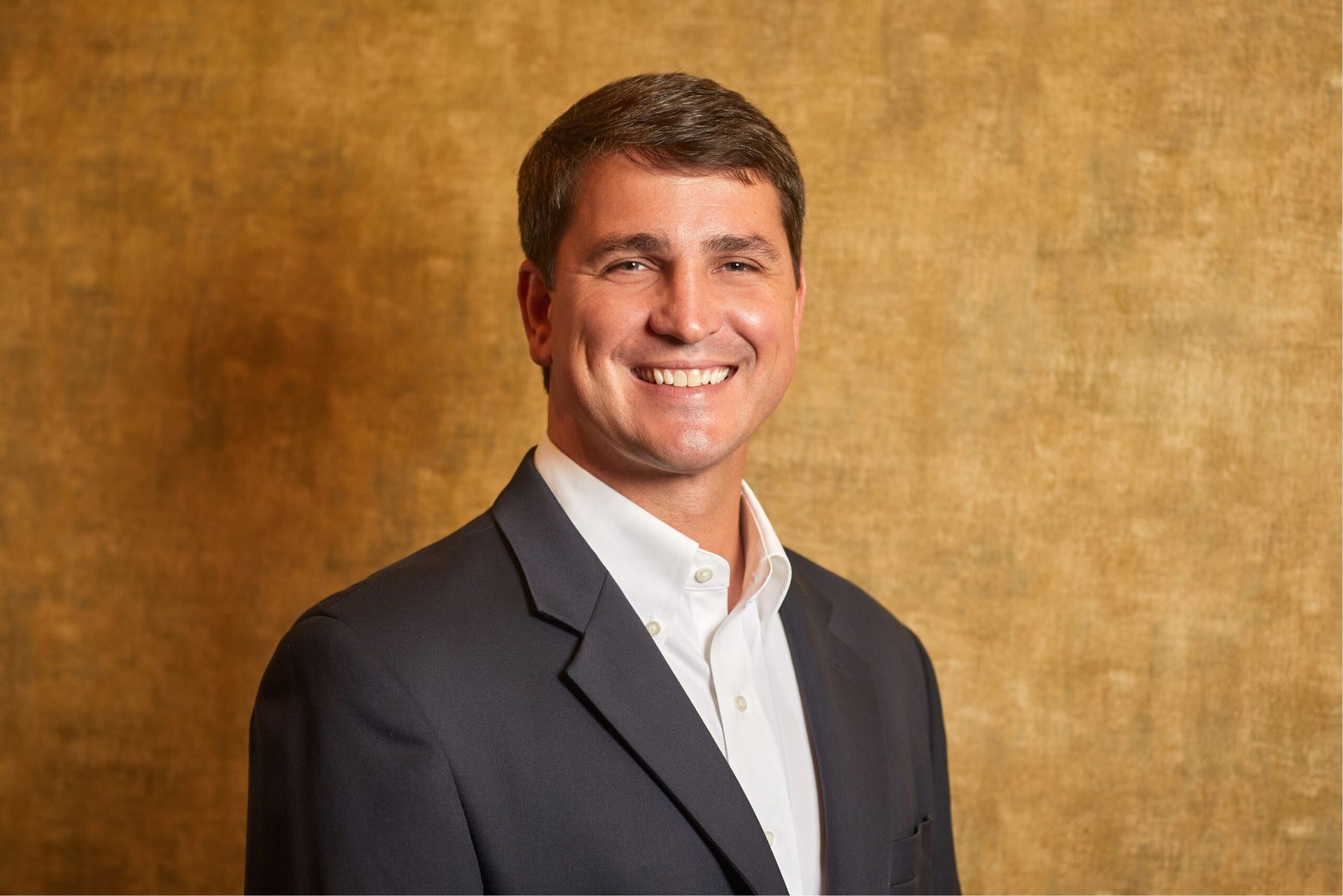 A man in a suit and white shirt is smiling for the camera.