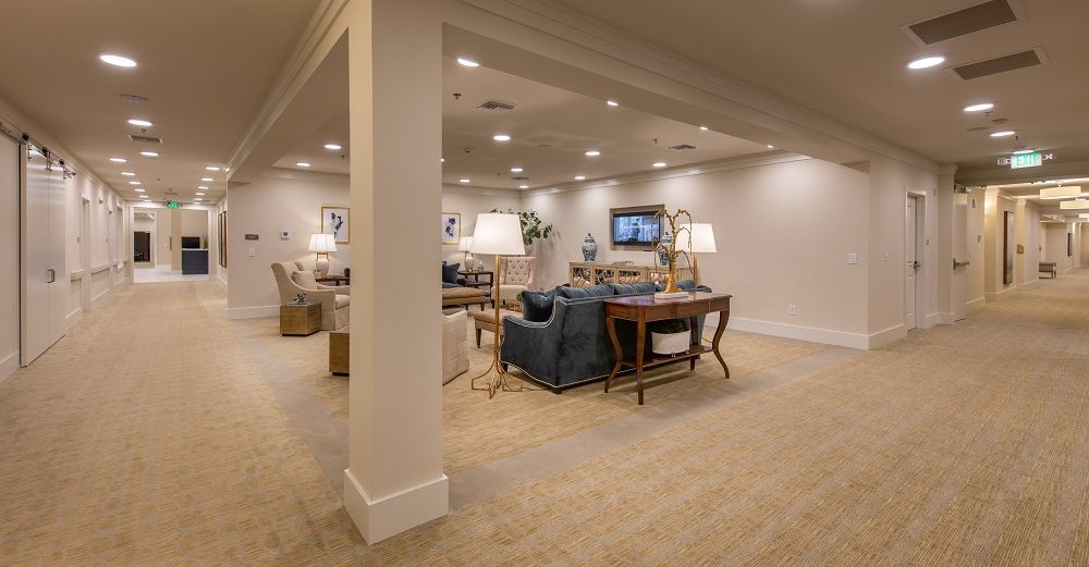 A long hallway with a couch , chairs , lamps and a television.