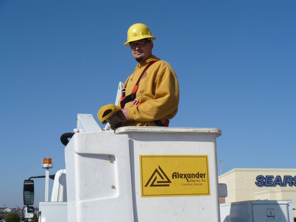A man wearing a hard hat is standing in a bucket that says alexander on it