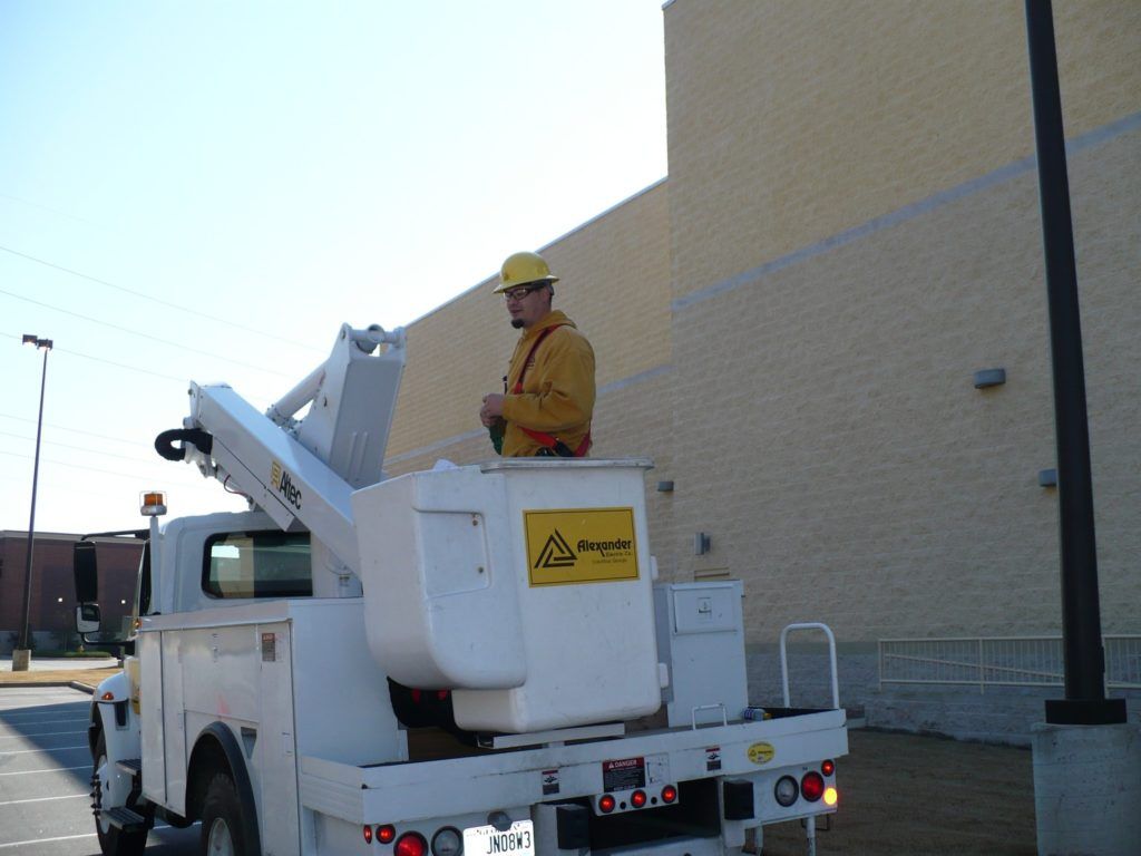A man in a yellow hard hat is sitting in the bucket of a utility truck