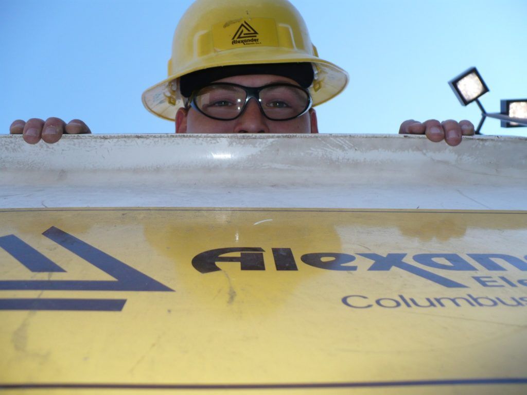 A man wearing a hard hat and glasses looks over a sign that says alexan