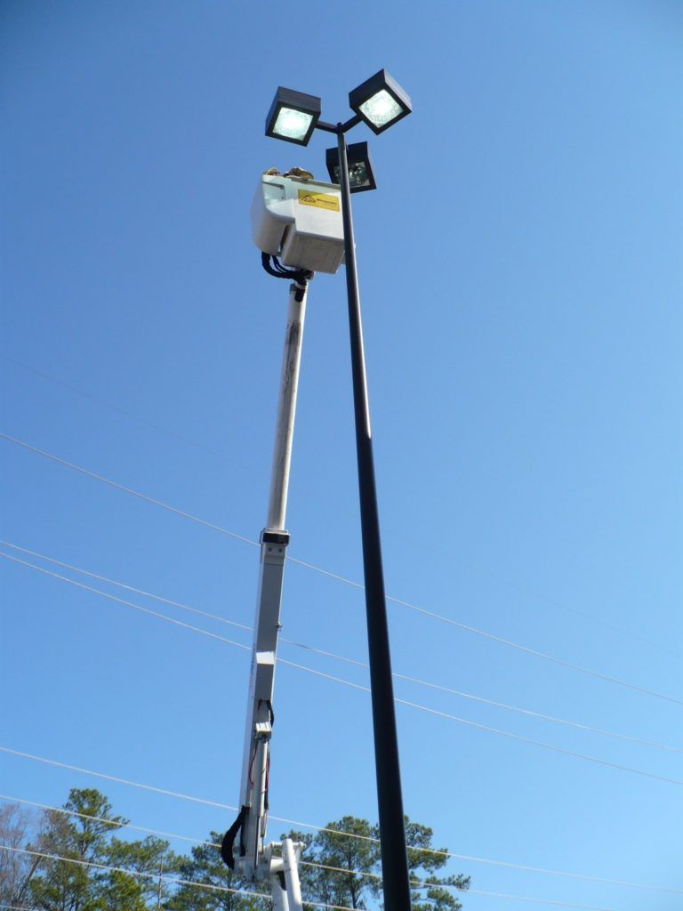 A crane is working on a street light with a blue sky in the background.