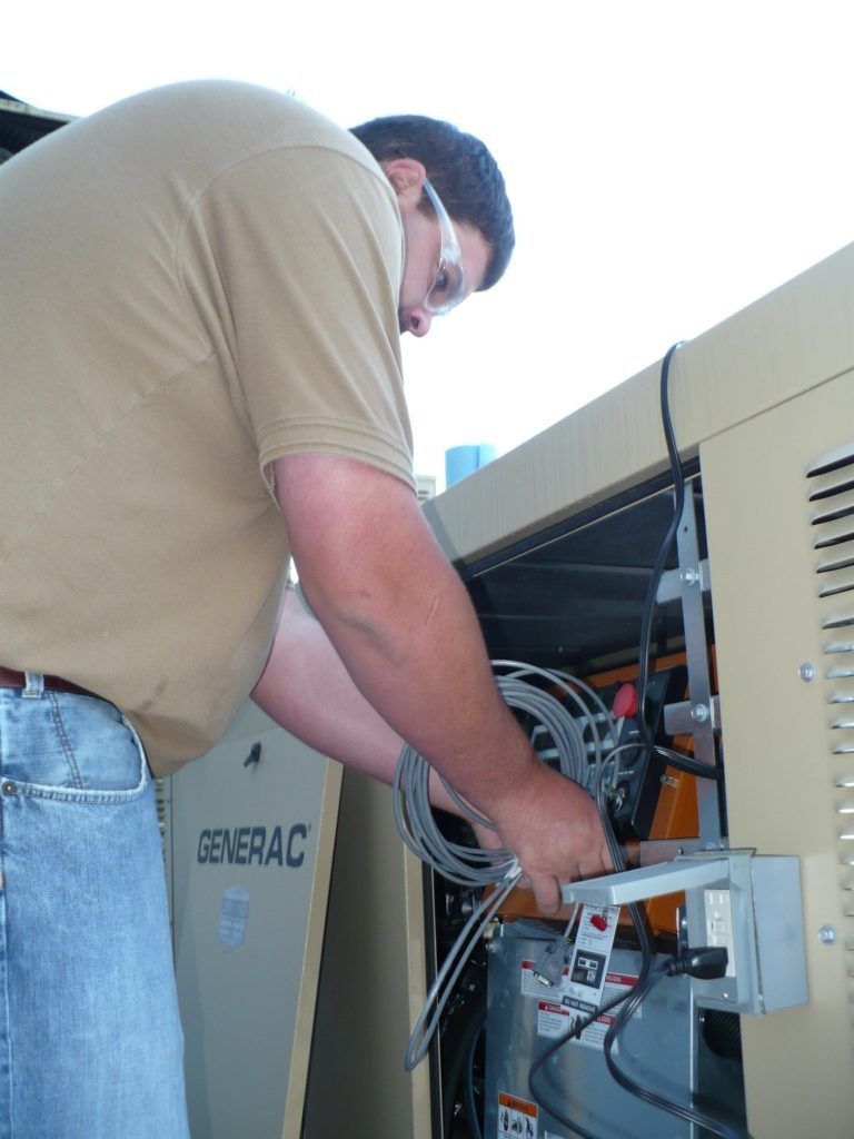 A man is working on a generator that says generac on it