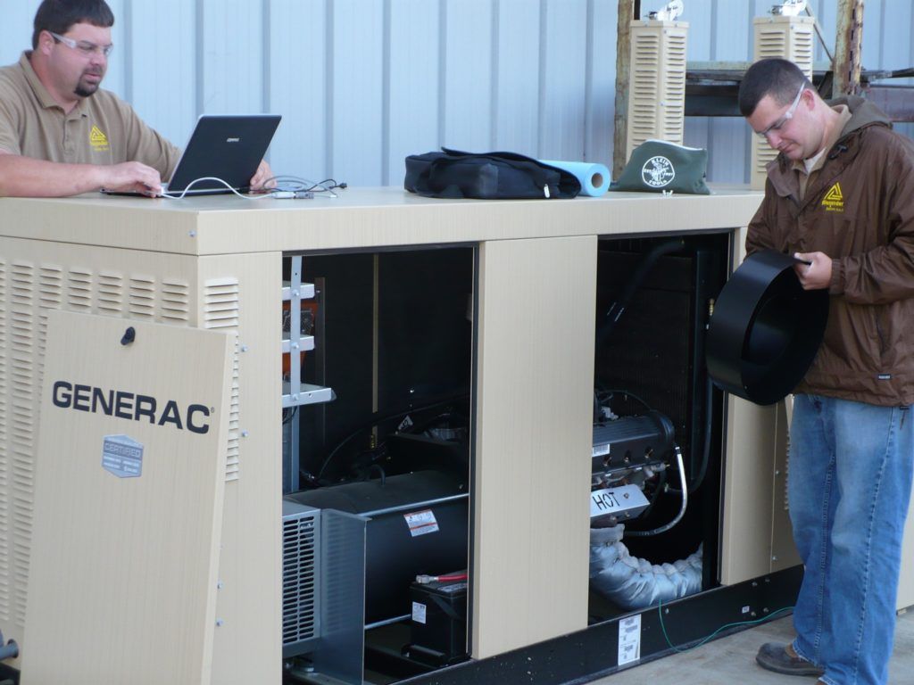 Two men are working on a generator and one is using a laptop