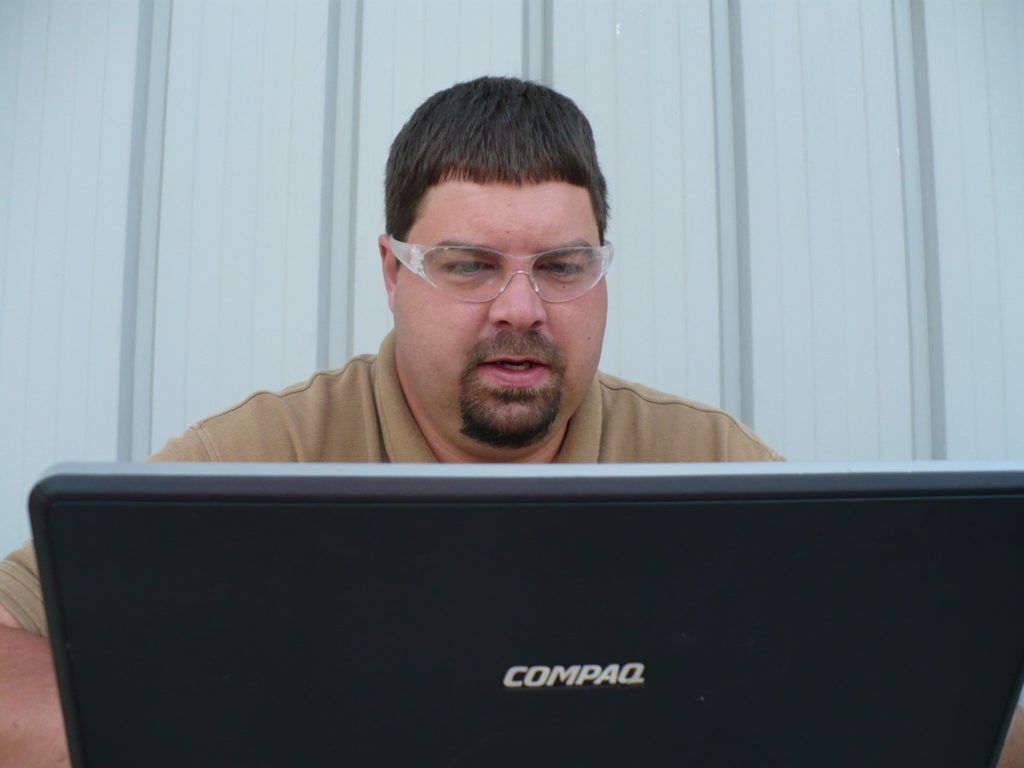 A man wearing glasses is looking at a compaq laptop