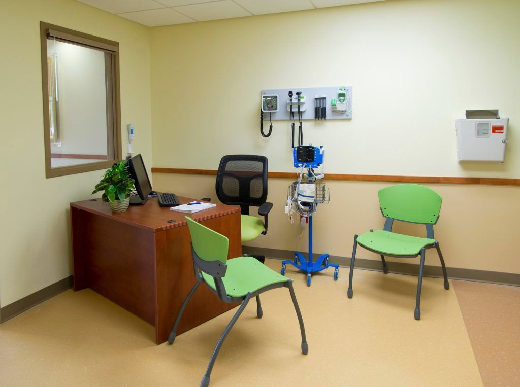 A doctor 's office with green chairs and a desk