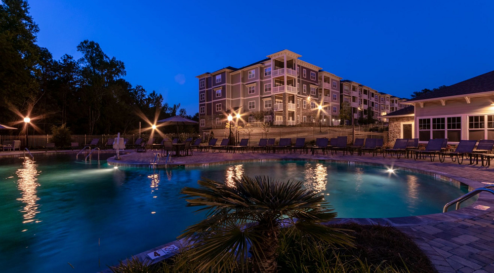 A large swimming pool is lit up at night in front of a large building.