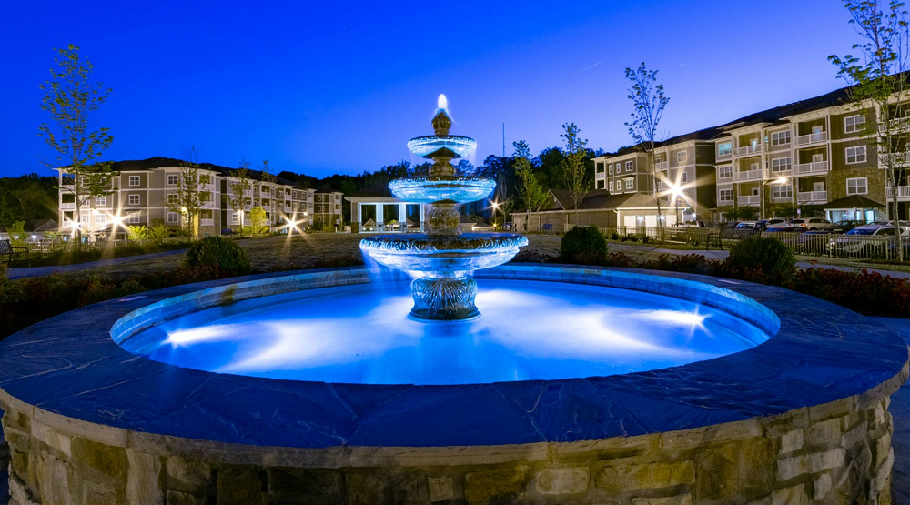 A fountain is lit up at night in front of a building.