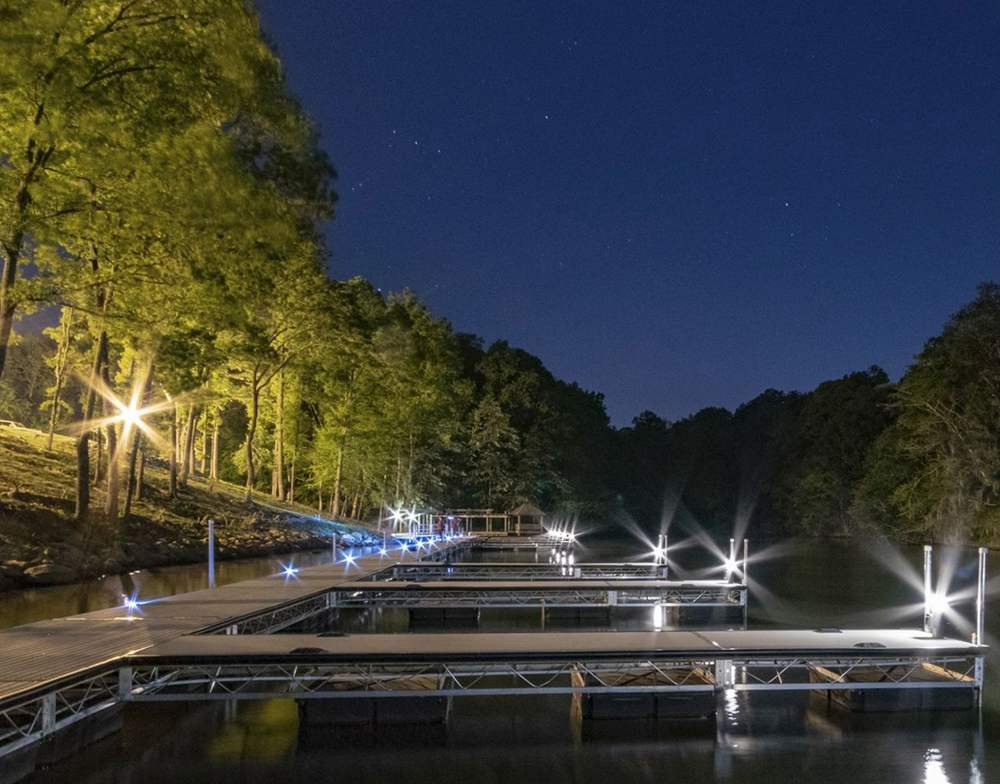 A dock is lit up at night on a lake surrounded by trees.