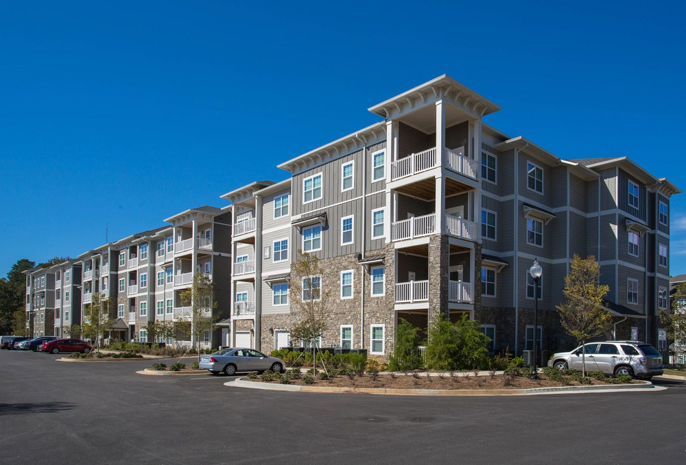 A large apartment building with cars parked in front of it on a sunny day.