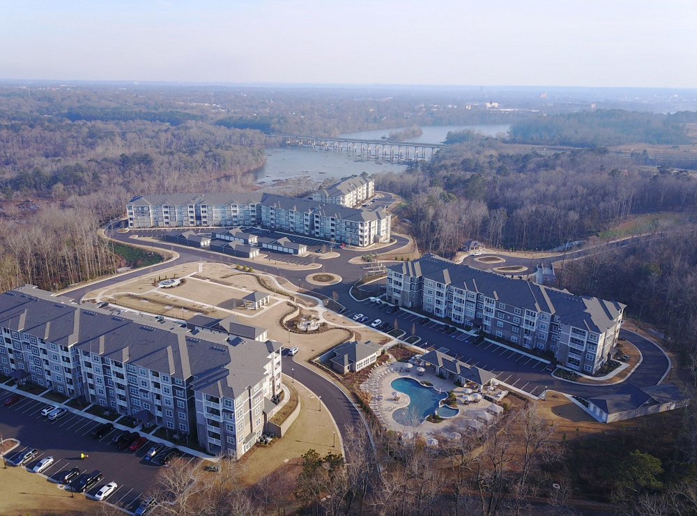 An aerial view of a large apartment complex surrounded by trees and a lake.