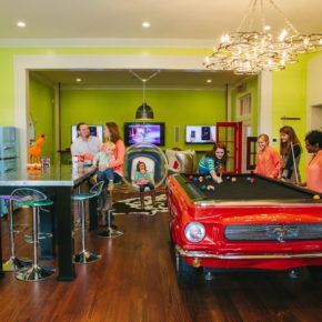 A group of people are standing around a pool table in a living room.