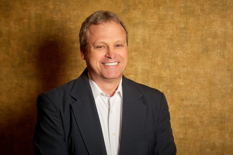 A man in a suit and white shirt is smiling for the camera.