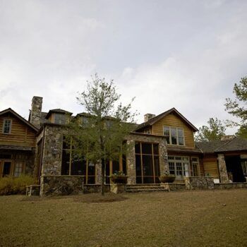 A large house with a lot of windows is surrounded by trees and grass.