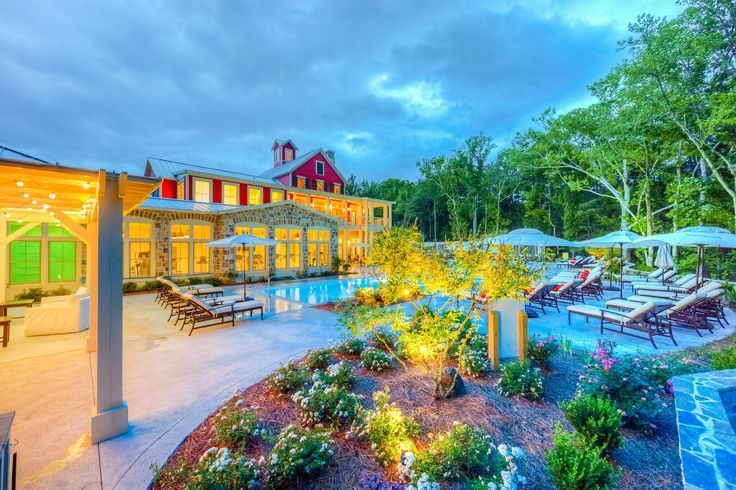 A large swimming pool surrounded by chairs and umbrellas in front of a large house.