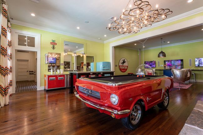 A pool table in the shape of a red car in a living room.