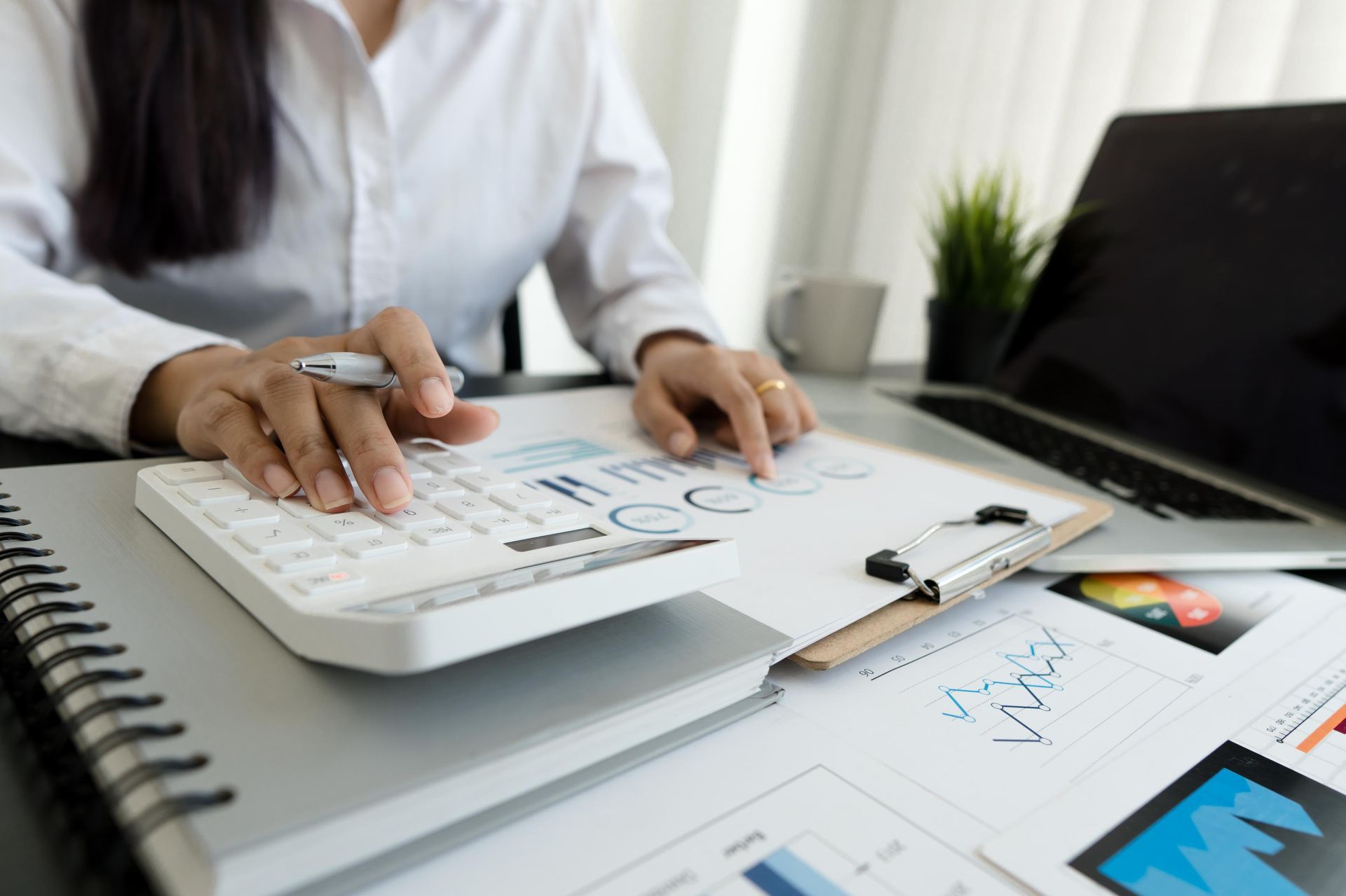 Person working at a desk with documents, calculator, laptop, and charts on a clipboard