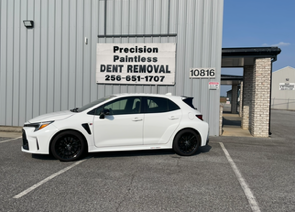 Person using a hammer to remove a dent from a car hood, working with a tool and cloth.
