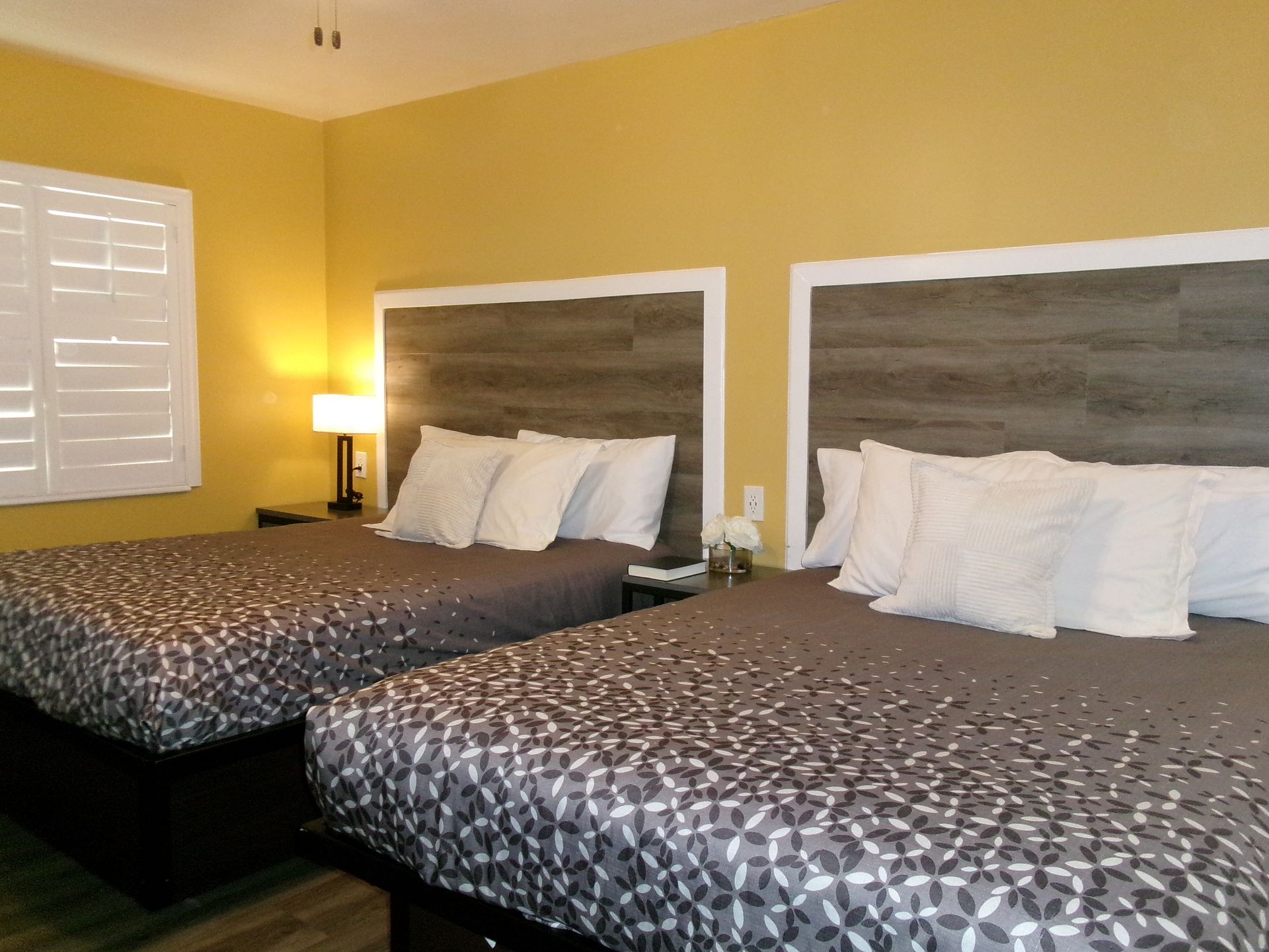 A hotel room with two queen beds featuring dark gray patterned comforters, wooden headboards, and yellow walls.