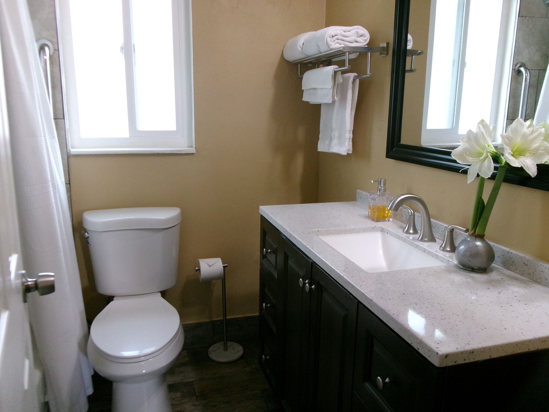 A small bathroom with tan walls, a white toilet, dark vanity cabinet with a speckled countertop, and white towels.